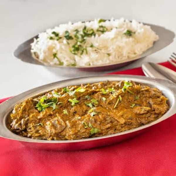 A silver platter of Indian curry with rice and cilantro, on a red tablecloth.