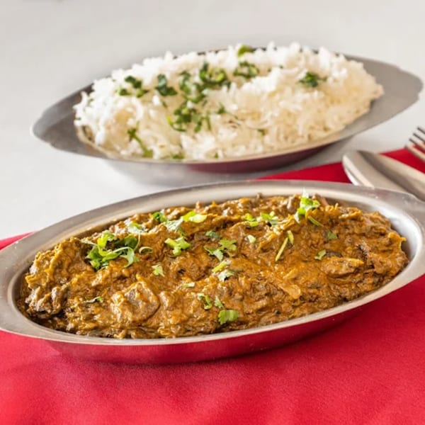 A metal dish of Indian curry with cilantro, and a separate dish of white rice with cilantro.