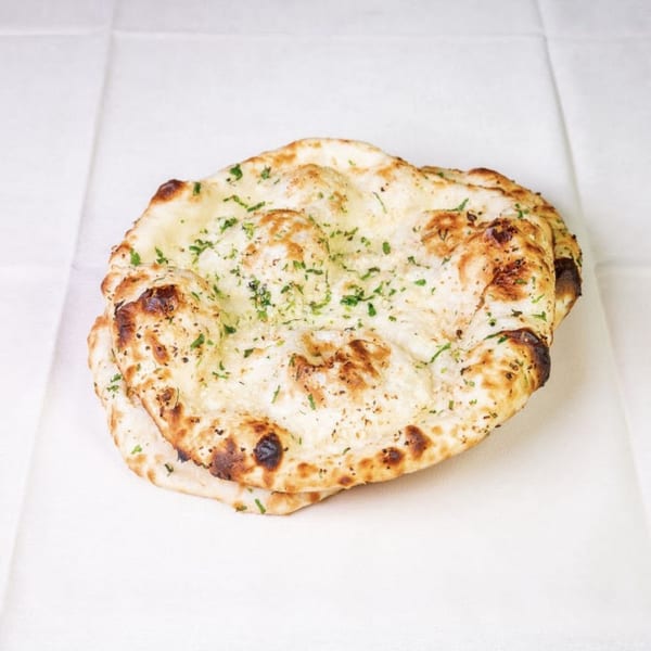 Two pieces of golden-brown naan bread, lightly charred and sprinkled with green herbs, on a white surface.