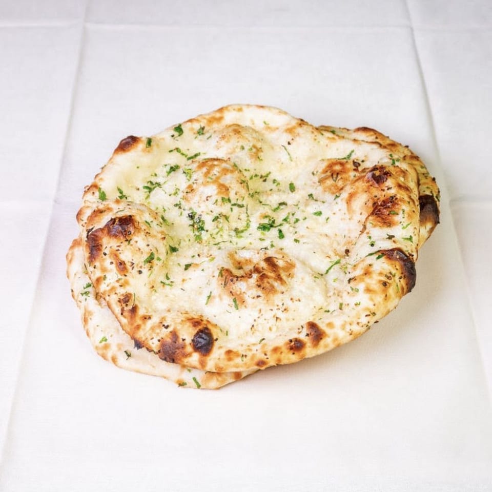 Two pieces of golden-brown naan bread, lightly charred and sprinkled with green herbs, on a white surface.