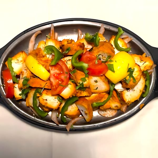 Sizzling chicken tikka with bell peppers, onions, tomatoes, and lemon wedges on a platter.