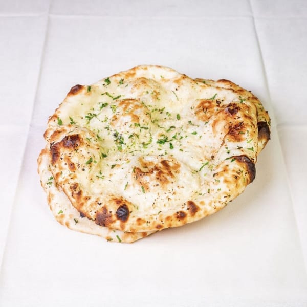 Two pieces of golden-brown garlic naan bread, sprinkled with green herbs, on a white surface.