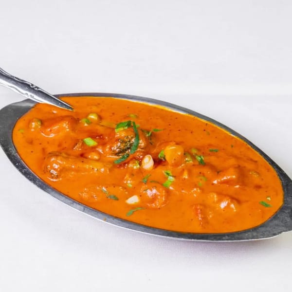 A silver serving dish filled with orange curry, garnished with green herbs and a spoon.