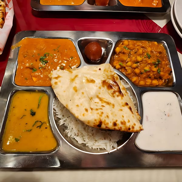 A stainless steel thali with various Indian dishes, including naan, rice, curries, and dessert.