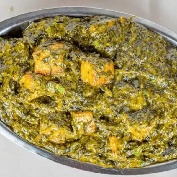 Palak Paneer, a vibrant green spinach curry with cubes of paneer cheese, served in a metal dish.